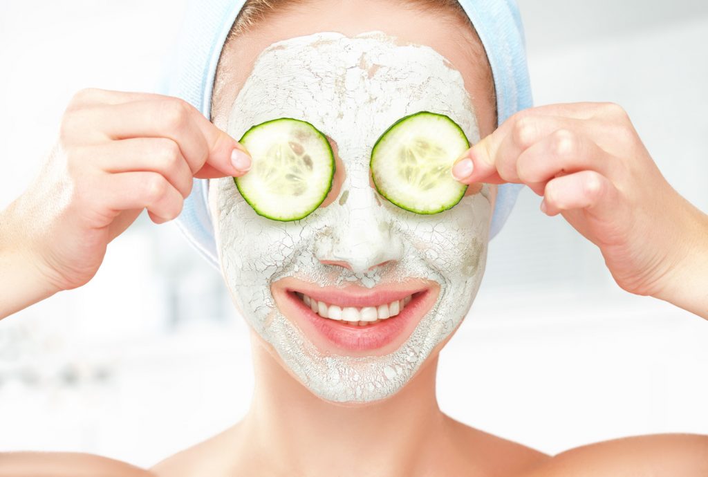 Funny young girl with a mask for skin face and cucumbers
